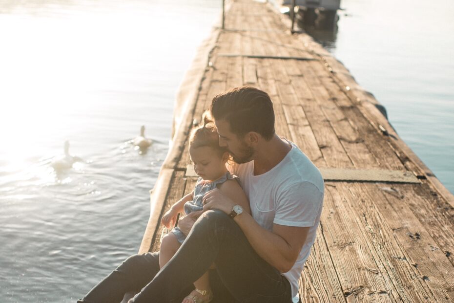 Ein Mann Und Ein Kind Sitzen Zusammen Auf Einem Holzsteg Am See Bei Sonnenuntergang